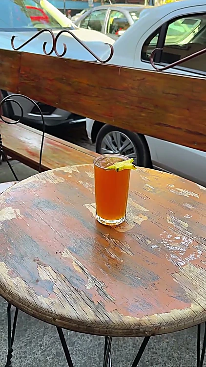 Bebida fría color ámbar con rodaja de cítrico en una mesa de la banqueta