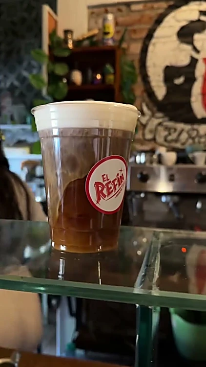 Bebida fría con espuma en vaso con el sello de El Refin, frente al mural