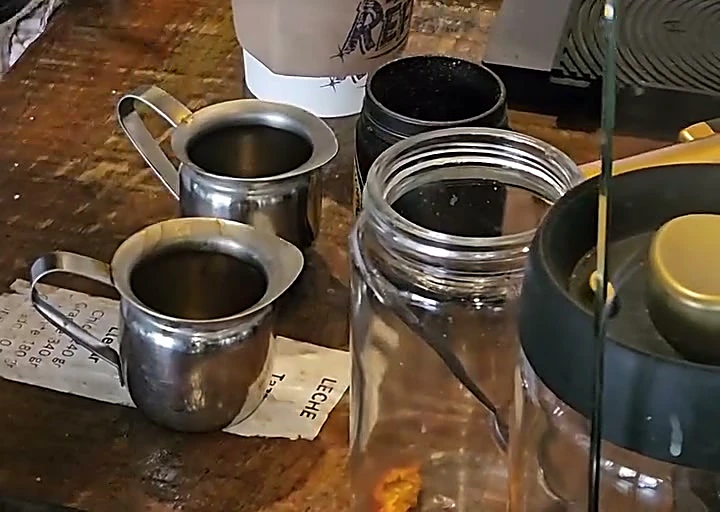 Jarritas de metal con café sobre la barra, listas para oler antes de preparar