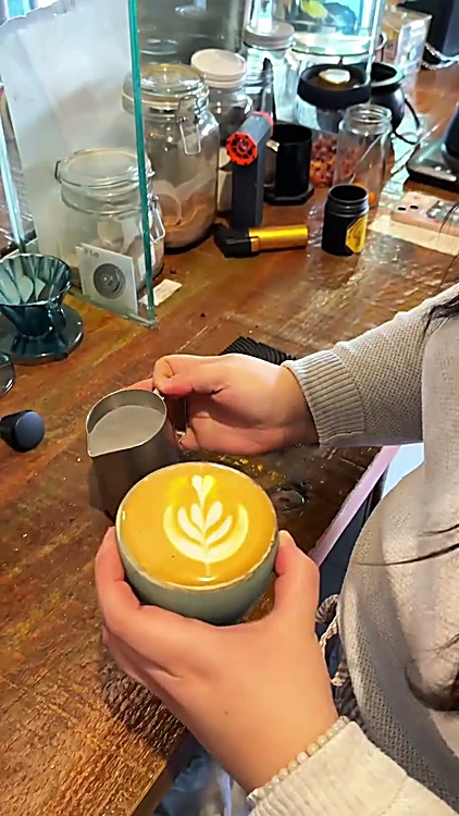 Manos sirviendo arte latte en una taza turquesa sobre la barra de madera
