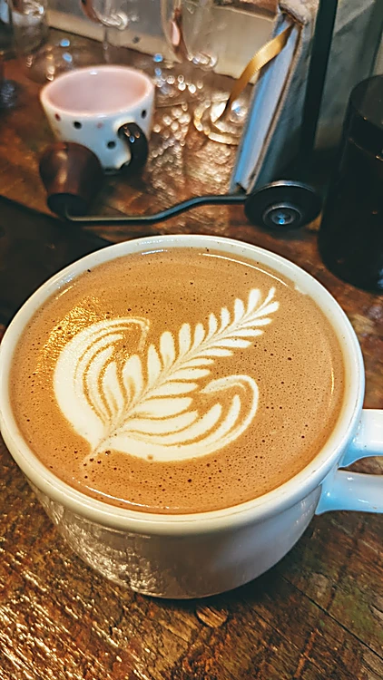 Latte con rosetta junto a una taza de lunares y un molino manual