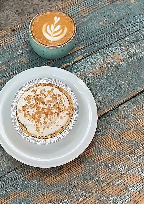 Latte en taza turquesa y un pay individual sobre una mesa azul gastada de la terraza